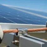 A close-up of an electrician securing a bare copper wire to a solar panel rail, demonstrating how to ground a solar power system safely.